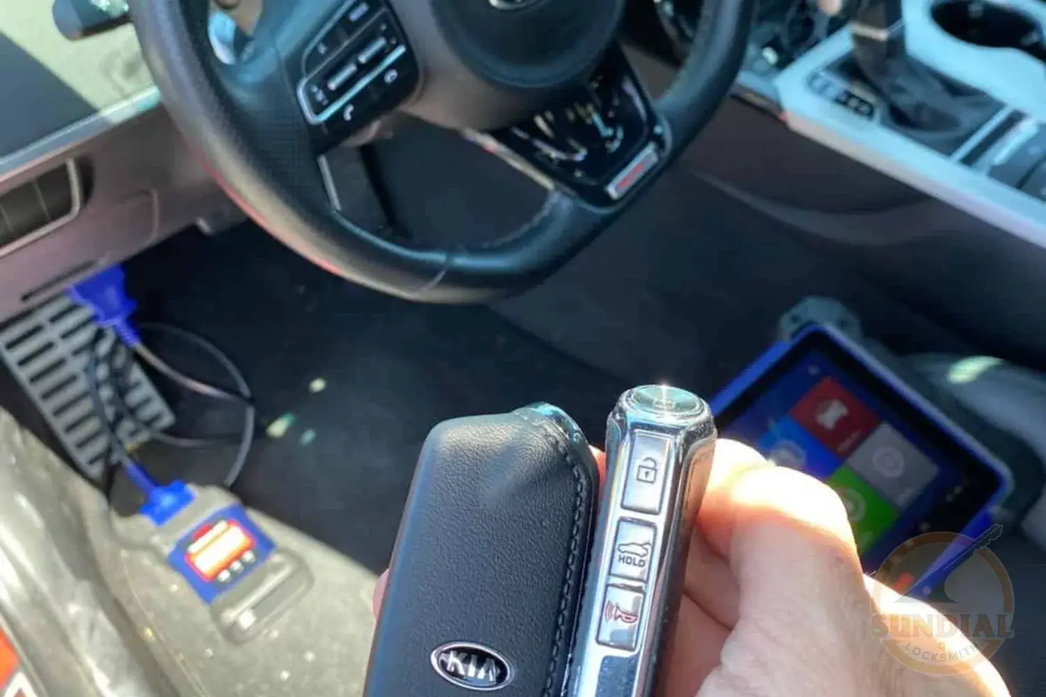 A close-up of a hand holding a Kia smart key with a car key programming device in the background.