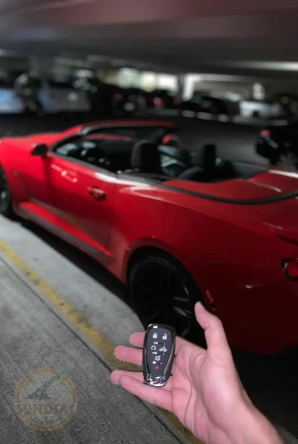A hand presenting a car key fob against the background of a sleek red sports car at night.