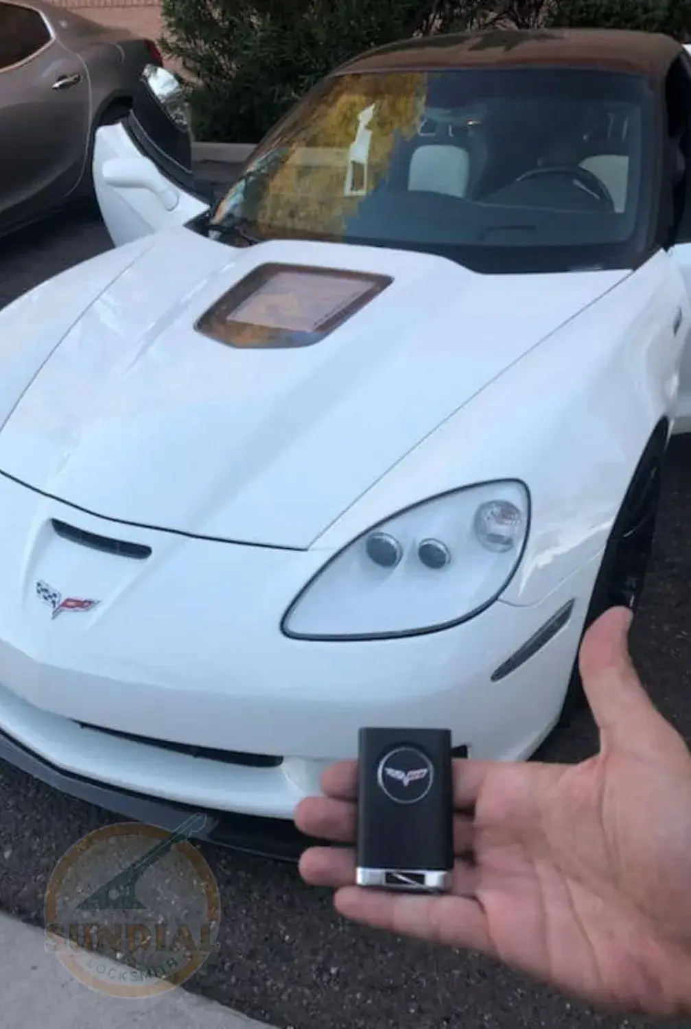 Hand holding a car key fob with a sports car in the background.