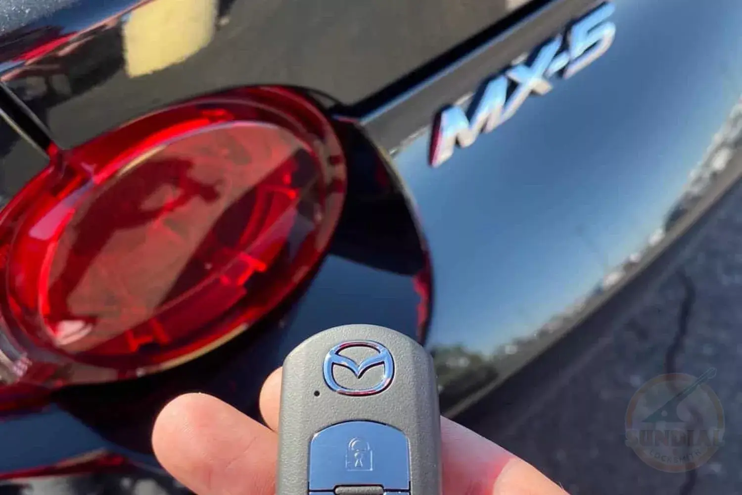 Close-up of a hand holding a new Mazda key fob with the MX-5 model emblem in the background.