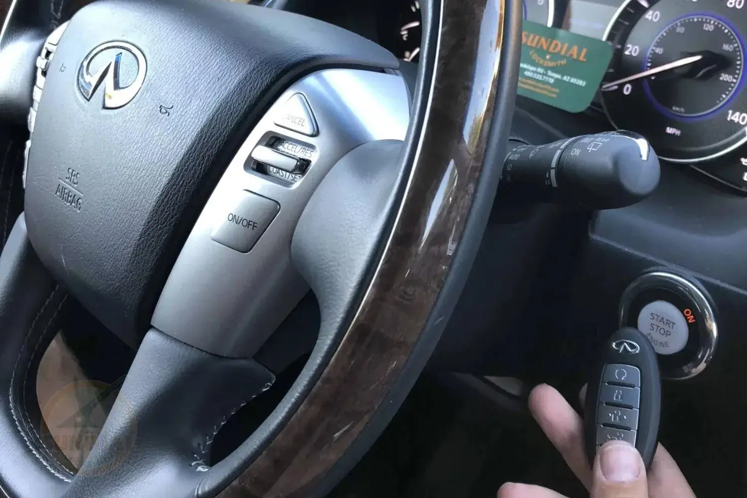 A driver's hand holding a car key fob near the start/stop engine button of a vehicle with a branded steering wheel in the background.