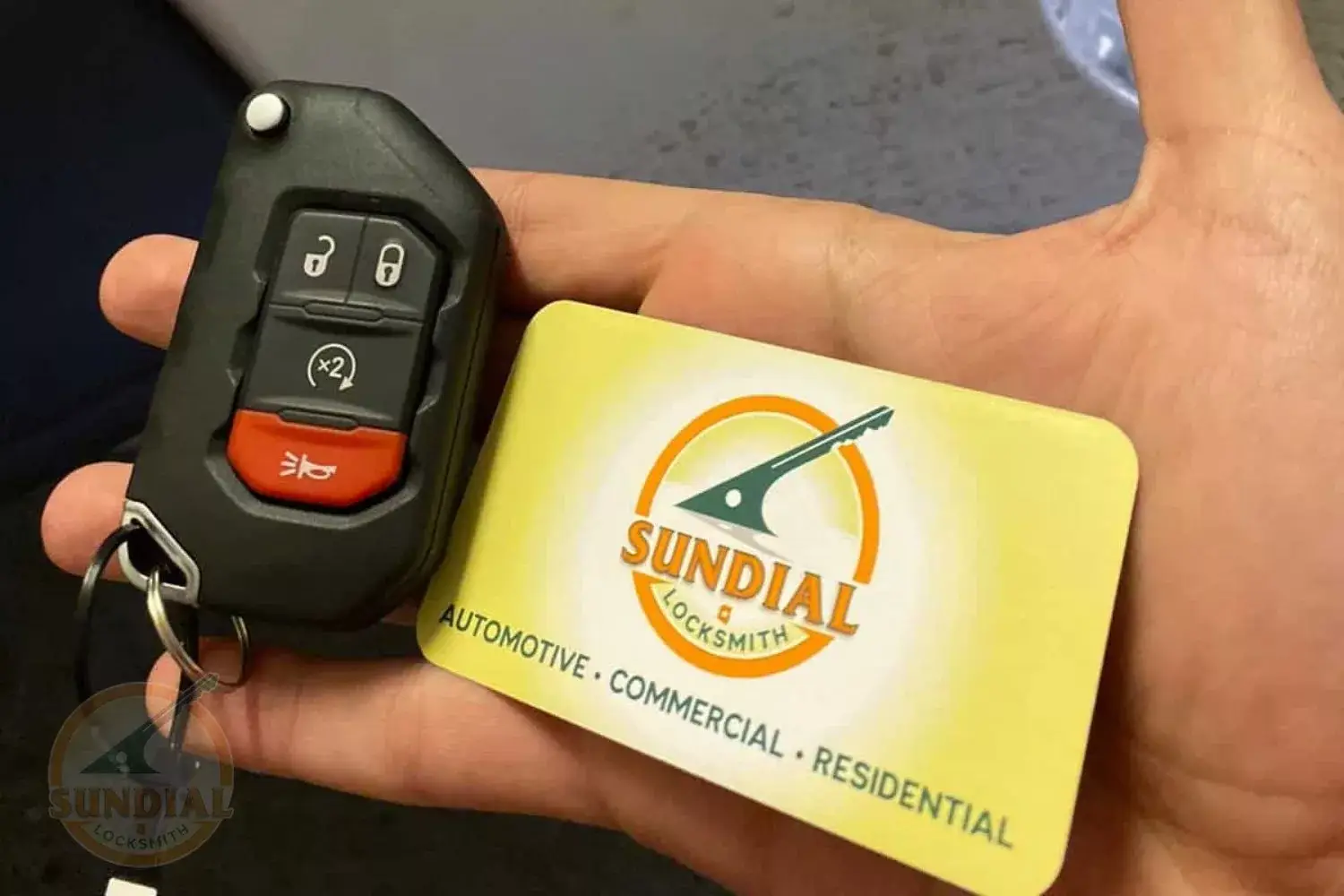 Hand holding car key fob and locksmith business card.