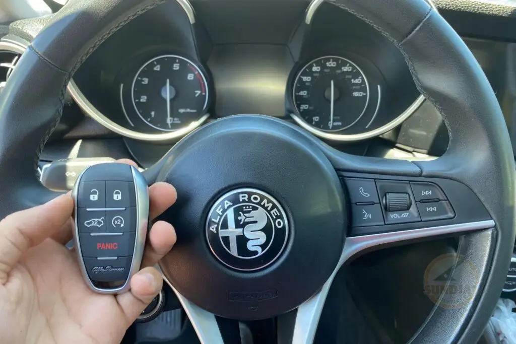 A close-up of an Alfa Romeo steering wheel with a hand holding the car's key fob in front.