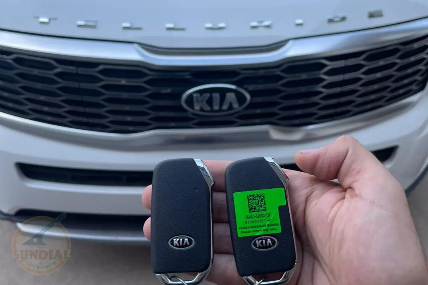 A pair of new Kia car keys held in front of a Kia vehicle's front grille.