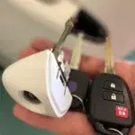 A hand holding several key fobs and keys, including one with a distinctive triangular white casing and a black car remote with buttons