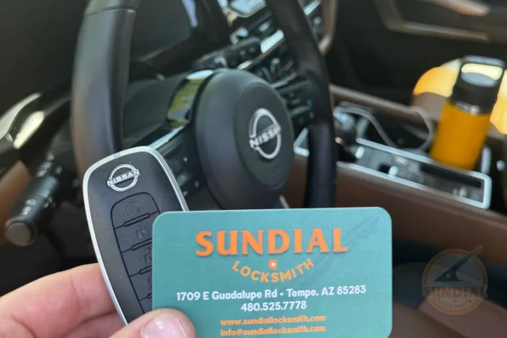 Nissan car key and Sundial Locksmith business card held in hand with car dashboard in the background.