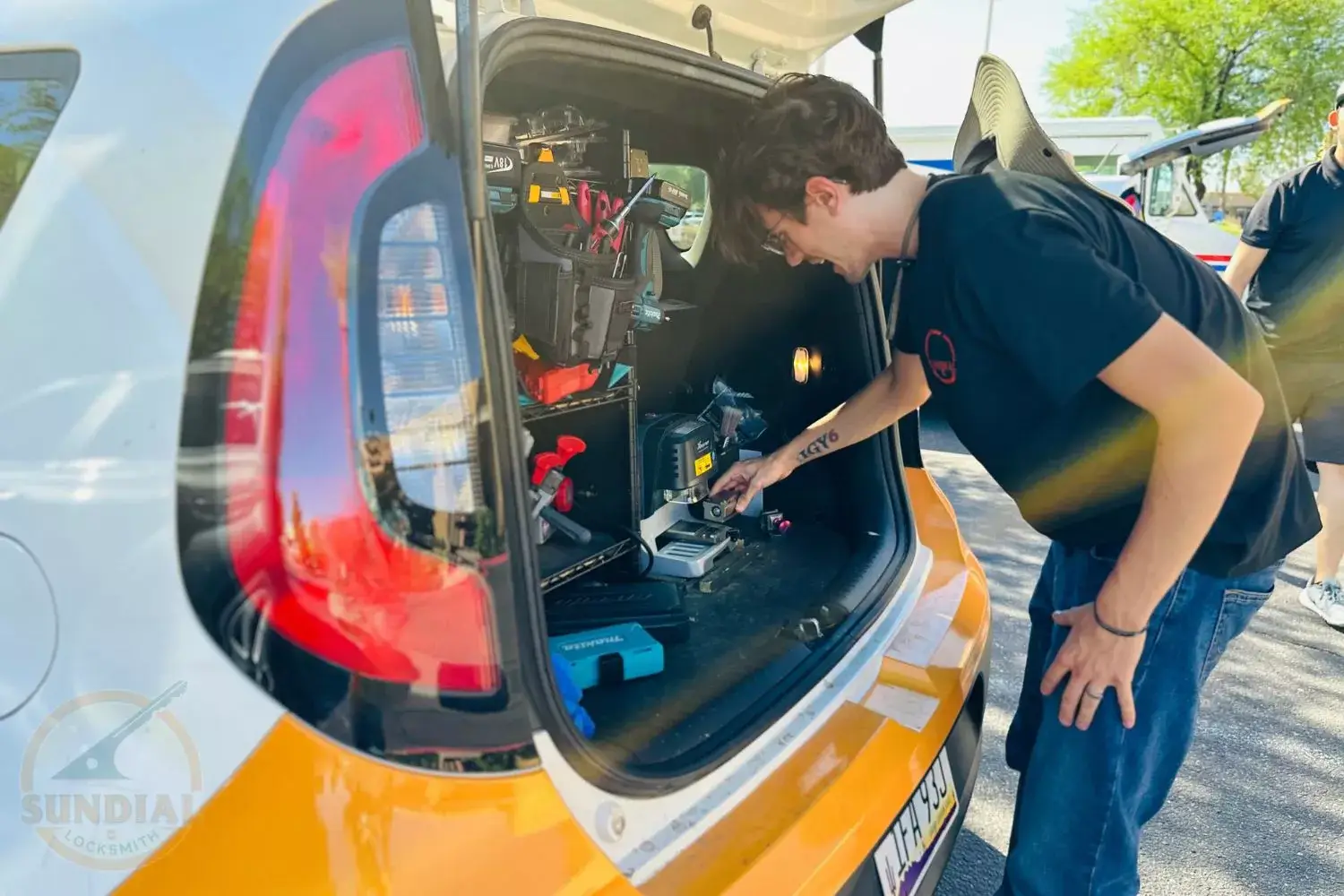 Locksmith working at the back of a parked car with tools and equipment spread out, with the 'Sundial Locksmith' logo visible.